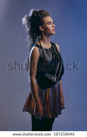 Rocker model girl with long hair in punk hairstyle, wearing black leather top and gold skirt on blue studio background