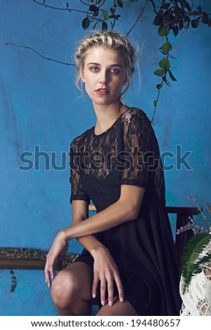 Beautiful blond woman with braid hairstyle and natural makeup. Wearing lace black dress. Against grunge blue background