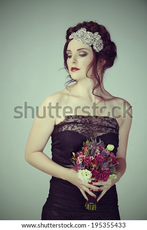 Beautiful brunette young model with braided hair with shiny crown wearing black lace dress in studio