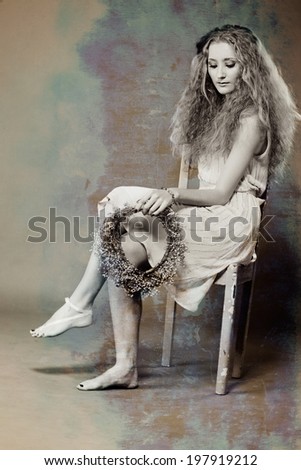 young woman with long blond curly hair and daisy flower wreath in a plain dress on studio background with grunge sepia texture