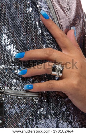 closeup of the woman's hand wearing luxury ring, blue gradient nail art manicure on silver sequin material background