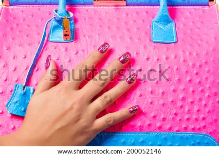 closeup of the woman\'s hand with bright art manicure, holding pink neon handbag with blue accents