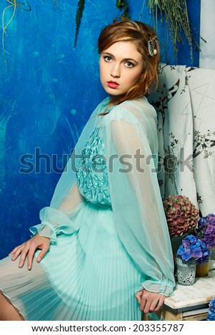 portrait of a beautiful woman with red hair in curly braided hairstyle. wearing a romantic blue turquoise dress on grunge blue background