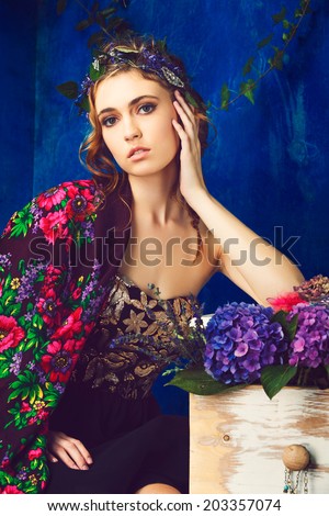 Beautiful brunette woman with braid hairstyle and natural makeup. Wearing black bohemian sequin corset dress. Against blue grunge background. Wearing flowers in her hairstyle