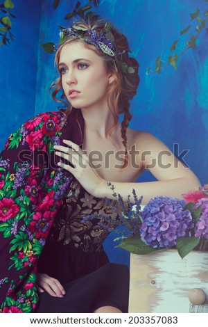 Beautiful brunette woman with braid hairstyle and natural makeup. Wearing black bohemian sequin corset dress. Against blue grunge background. Wearing flowers in her hairstyle