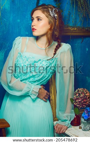 portrait of a beautiful woman with red hair in curly braided hairstyle. wearing a romantic blue turquoise dress on grunge blue background