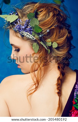 portrait of a beautiful woman with red hair in curly braided hairstyle wearing a crown of fresh flowers