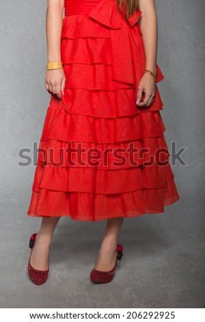 closeup of woman wearing red ruffled skirt and shoes on grunge studio background, wearing antique jewellery