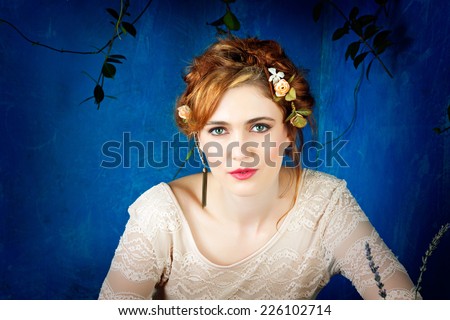 Romantic portrait of a beautiful woman with red hair and flowers in her hairstyle, wearing diamond ear cuff against blue grunge background