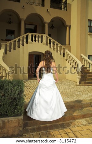Beautiful bride, brown hair, with her back on the stairs of a Tuscan style house, in natural light
