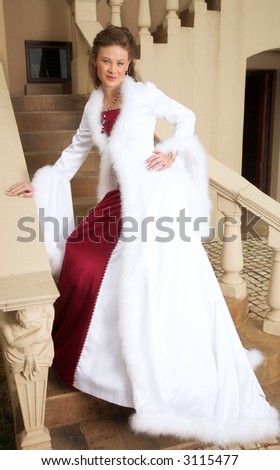 Beautiful smiling bride in red and white satin dress with feather coat, on the stairs