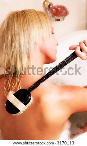 Young blond woman sitting in bath with body brush on her back