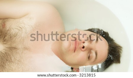 Young man in the bath with whole body under clean body and face is out. Focus on the eyes, shallow DOF