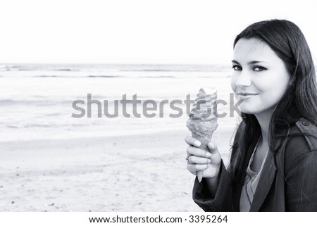 Beautiful woman with long dark hair smiling with caramel ice-cream on beach, blue sepia