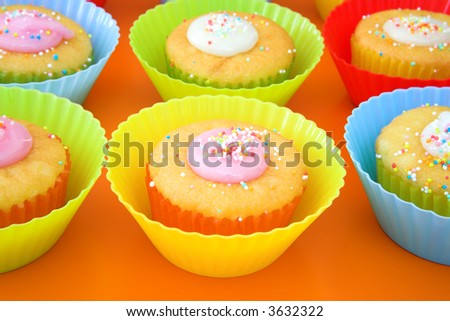 Display of small party cakes with icing sugar in bright plastic cups. Focus on middle cake