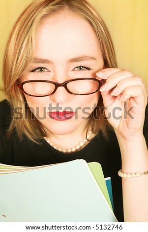 Blond businesswoman in black with pearls squinting over brown glasses in doubt, holding files