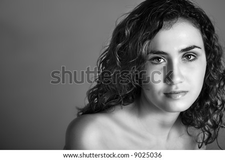 Portrait of a beautiful woman with brown curly hair and natural makeup in low-key black and white effect and visible clear skin texture