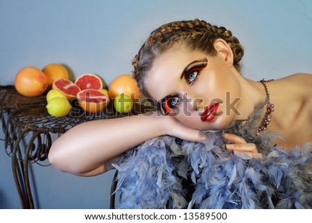 beautiful woman with long feather lashes and feather boa resting on a chair with fruit in the background