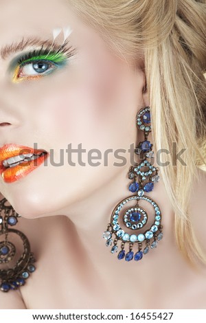 Beautiful blond woman with bright orange lips and false feather lashes in diamante chandelier earrings