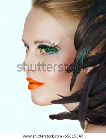 beautiful woman with artistic gold and orange lips and green eyelashes with feathers on white background