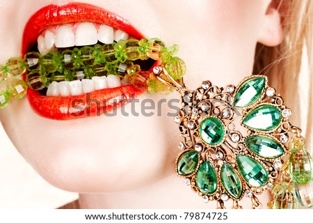 woman with bright red lips biting on emerald green expensive necklace with her teeth