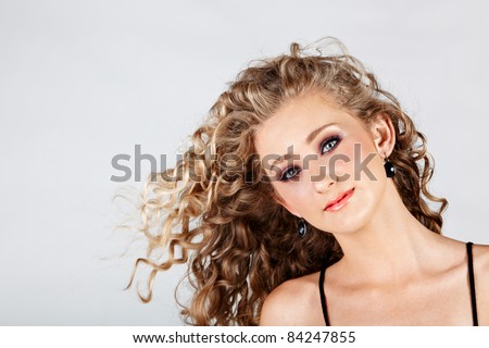 beautiful strawberry blond happy teenage girl with green eyes and long curly hair blowing in wind over grey studio background .