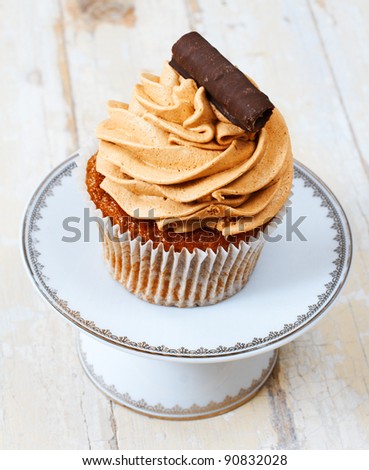 Coffee and chocolate cream cupcake with a swirl on a white plate against grunge wooden background.