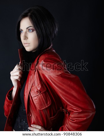 beautiful young brunette woman wearing red leather jacket on black studio background.