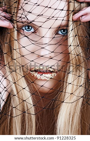 portrait  of a beautiful blond woman with long hair and gold leaf on sensual lips holding net veil before her face