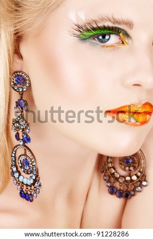 Close-up fashion portrait of a sensual beautiful blond woman model face with bright make-up, long eyelashes and luxury earrings.
