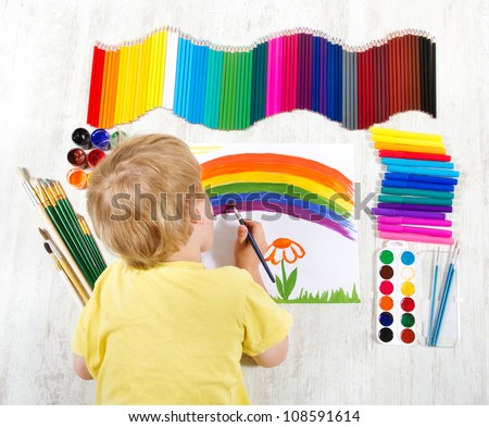 Child painting picture with brush in album using a lot of painting tools. Top view. Creativity concept.
