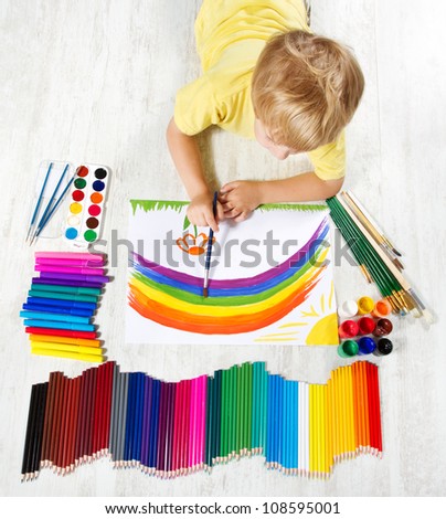 Child painting picture with brush in album using a lot of painting tools. Top view. Creativity concept.