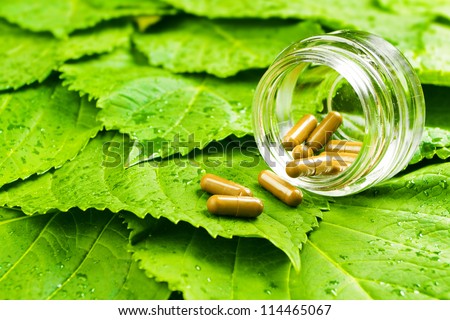 Pills in jar over green leaves. Healthy vitamin concept