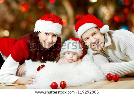 Christmas family of three persons in red hats. Happy parents and small funny baby