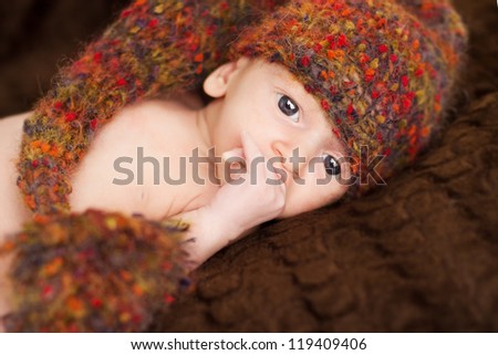Newborn baby close up portrait in woolen hat, new born on brown background