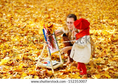 Mother and child drawing on easel in autumn park. Creative kids development concept.