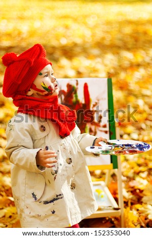 Child drawing on easel in Autumn Park. Creative kids development concept.