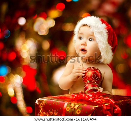 Christmas baby in santa hat holding red ball near present gift box