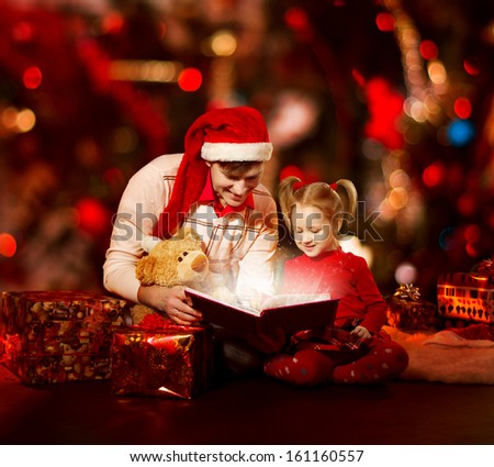 Christmas family reading book. Father and child opening magic fairy tale over red background.