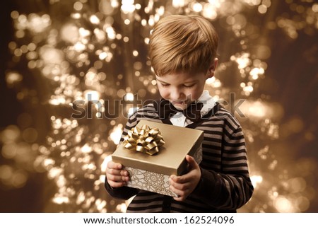 Child holding present gift box. Boy in vintage style smart casual clothing, brown colors.