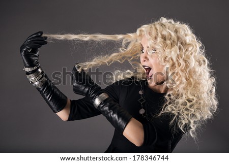 curly hairstyle blonde in black, woman hairs loss, coloring problem, beautiful girl holding hairs and surprised, over gray background