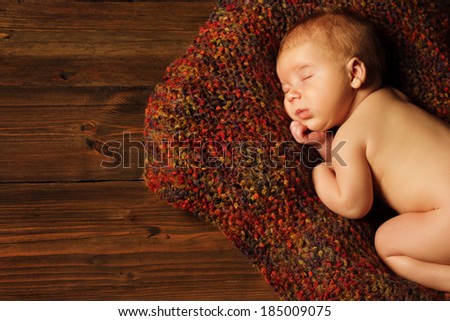 baby newborn portrait, new born kid sleeping in woolen blanket on brown wooden background