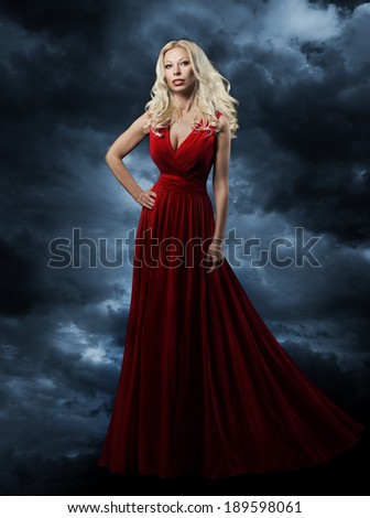 Woman in red dress, long hair blonde in fashion evening gown over sky background, hand on hip