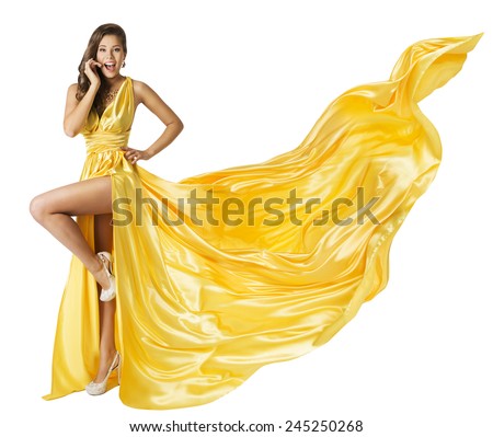 Woman Beauty Fashion Dress, Beautiful Girl In Flying Yellow Fluttering Gown, Standing on One Leg High Heels, Surprised with Open Mouth. Fabric Cloth Waving on Wind, Isolated Over White Background