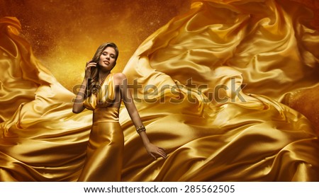Fashion Model in Gold Dress, Beauty Woman Posing over Flying Waving Cloth, Girl with Yellow Dynamic Silk Fabric