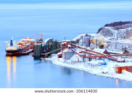 Industrial Container Cargo freight ship with working crane bridge in shipyard at Iron Ore Mine Factory Plant in Narvik Norway