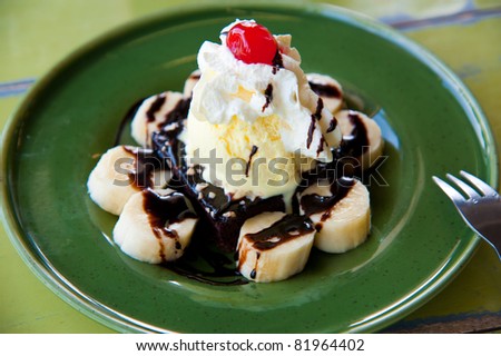 one scoop of vanilla ice-cream topping with banana, cream, red jelly and chocolate