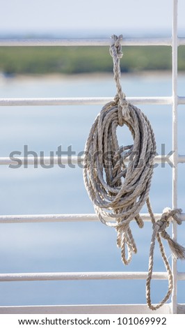 Length of rope tied to white railings on ship with water and land in background
