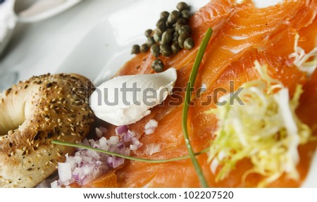 A platter of smoked salmon with a toasted everything bagel garnished with red onion, scallion, cream cheese and capers