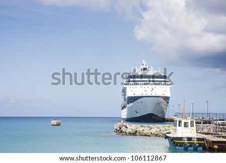 A blue and white cruise ship tied to a pier near a pilot boat on a tropical island